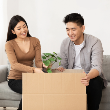 Happy man and happy woman unpacking green plant from cardboard box in new home